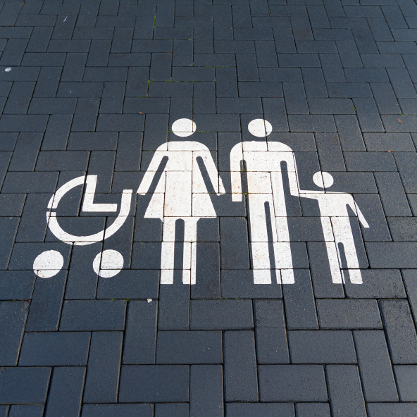 Biały rysunek na chodniku przedstawiający wózek, kobietę i mężczyznę, który trzyma za rękę dziecko.