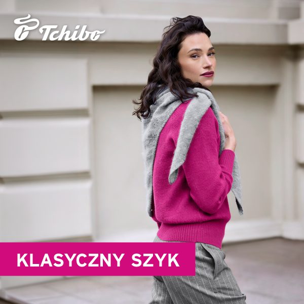 Modelka w różowym swetrze, szarej chuście i szarych spodniach w prążki. Kolekcja Tchibo „Klasyczny szyk”.
