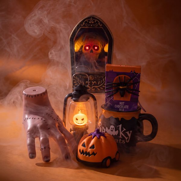 Dekoracje Halloween w Rossmannie: sztuczna ręka, dzwonek z czaszką, latarnia z dynią, pojazd w kształcie dyni oraz kubek z czekoladą do picia.